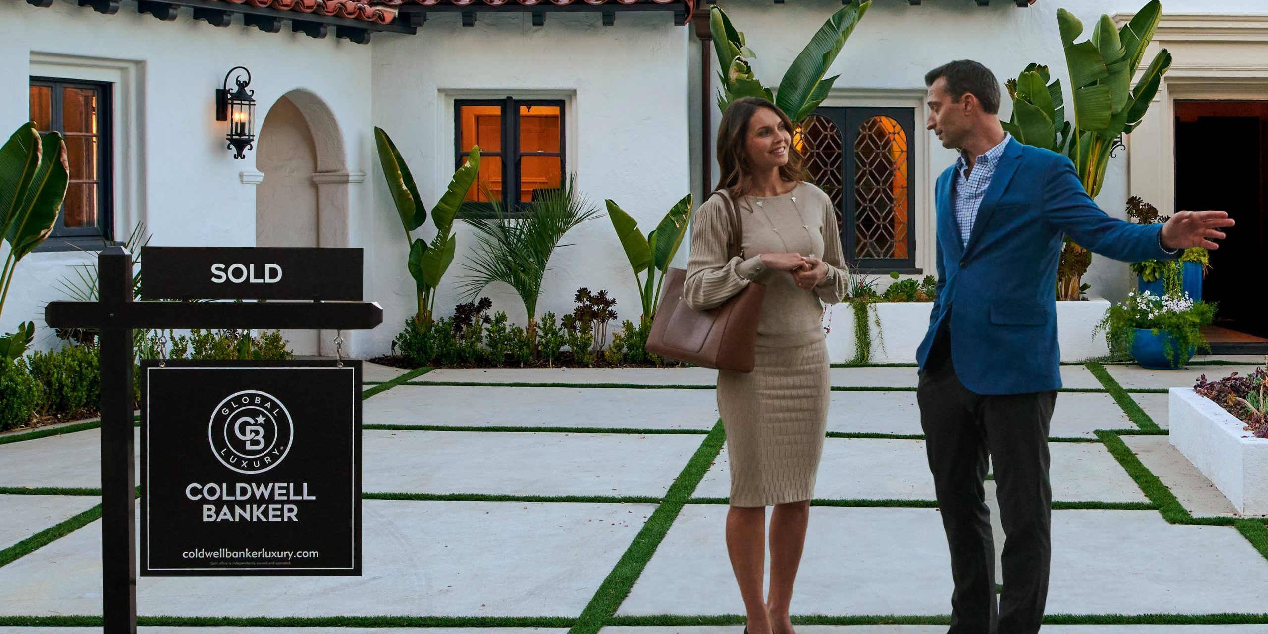 Real estate agents having a discussion in a front lawn of a house with a Coldwell Banker Global Luxury Signage